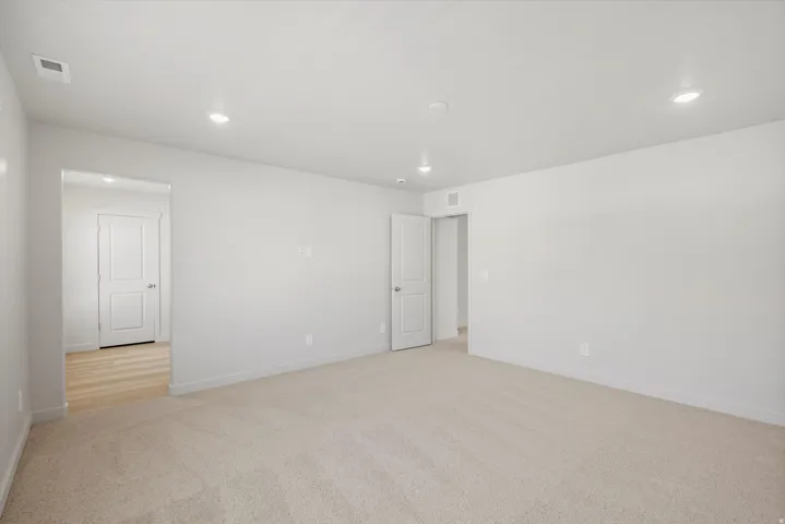 Spacious room featuring neutral carpeting, light-toned walls, recessed lighting, and white trim