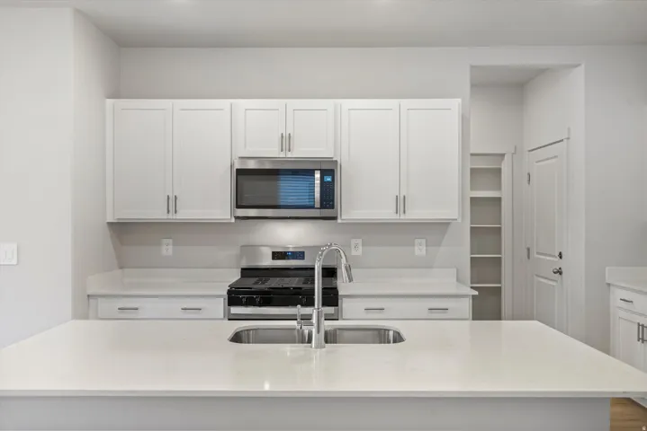 Kitchen featuring white shaker-style cabinetry, stainless steel appliances including a microwave and range, light-toned countertops, and a double basin sink