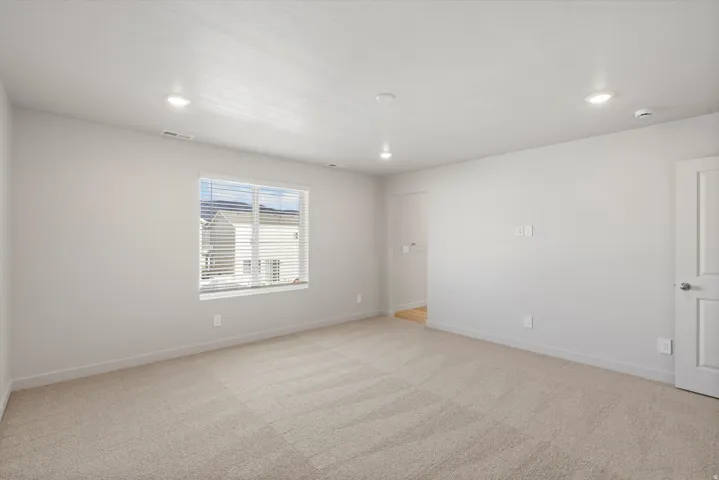 Spacious room with plush carpeting, recessed ceiling lighting, a large window with horizontal blinds, and a paneled interior door