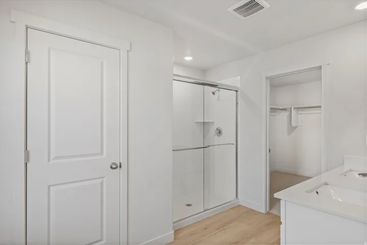 Contemporary bathroom featuring a spacious glass-enclosed shower, white subway tile surround, recessed lighting, wood-finish flooring, and a walk-in closet with built-in shelving