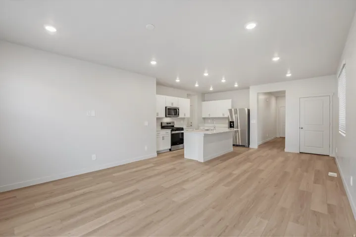 Open-concept living space featuring wood-finish flooring, recessed lighting, and a kitchen with white cabinetry, a kitchen island, and stainless steel appliances