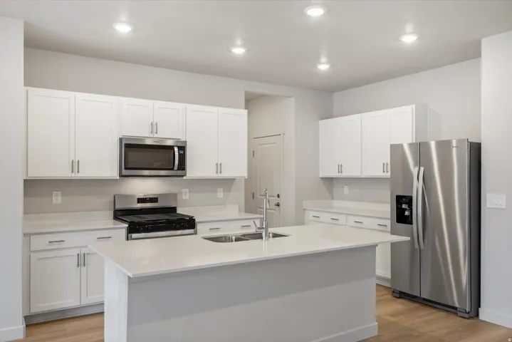 Bright kitchen featuring white cabinetry, stainless steel appliances, a center island with double basin sink, light countertops, and wood-finish flooring