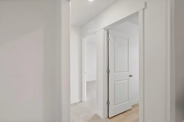 Interior hallway featuring recessed ceiling lighting, light-toned carpeting, and a white paneled door with a brushed nickel knob