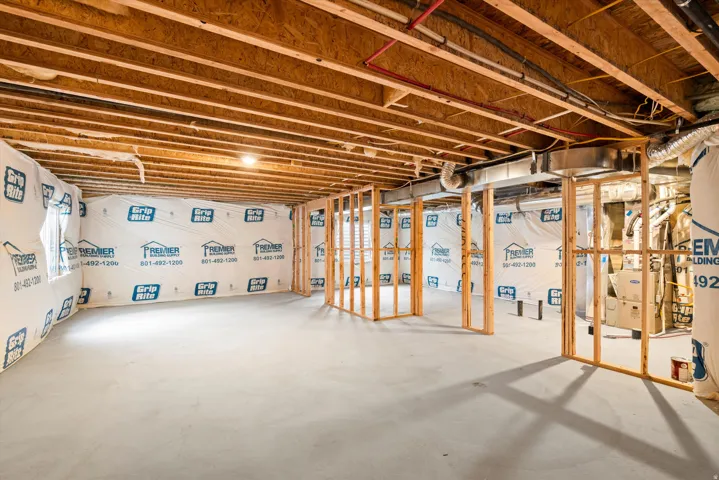 Unfinished basement featuring exposed wood joists and subfloor, concrete flooring, and framed walls