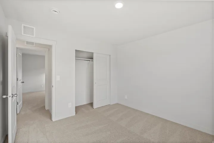 Carpeted room featuring a white interior color palette, recessed lighting, and a sliding door closet with built-in hanging rod