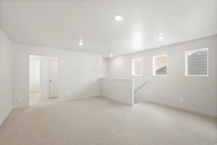 Open concept bonus room featuring light neutral wall paint, recessed lighting, neutral carpet, three windows, and a staircase with a white railing