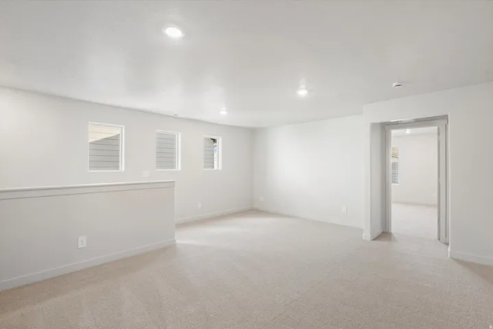Spacious carpeted room featuring recessed lighting, multiple windows, a half-wall partition, and an open doorway