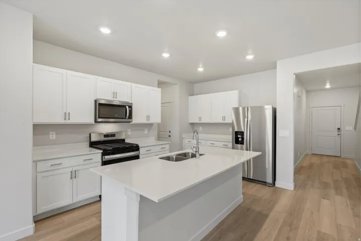 Modern kitchen featuring white cabinetry, stainless steel appliances, light-colored countertops, a center island with an undermount sink, and wood-finish flooring