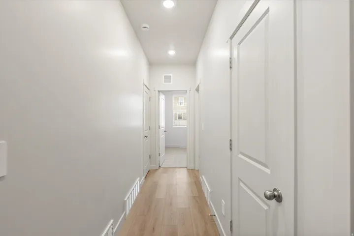 Hallway featuring light wood-finish flooring, recessed lighting, white interior doors with satin nickel hardware, and white wall finishes