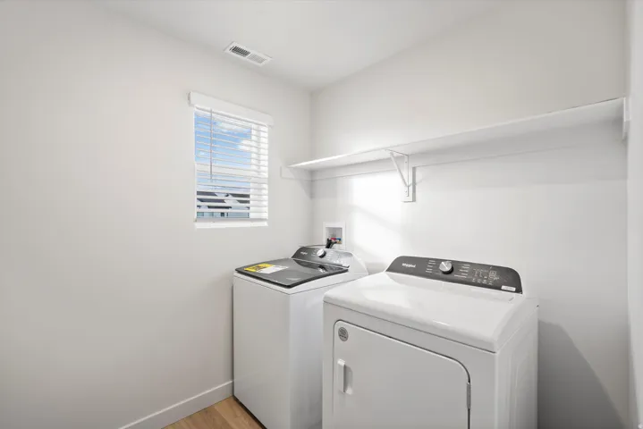 Dedicated laundry area featuring a window with blinds, upper shelving, and wood-finish flooring