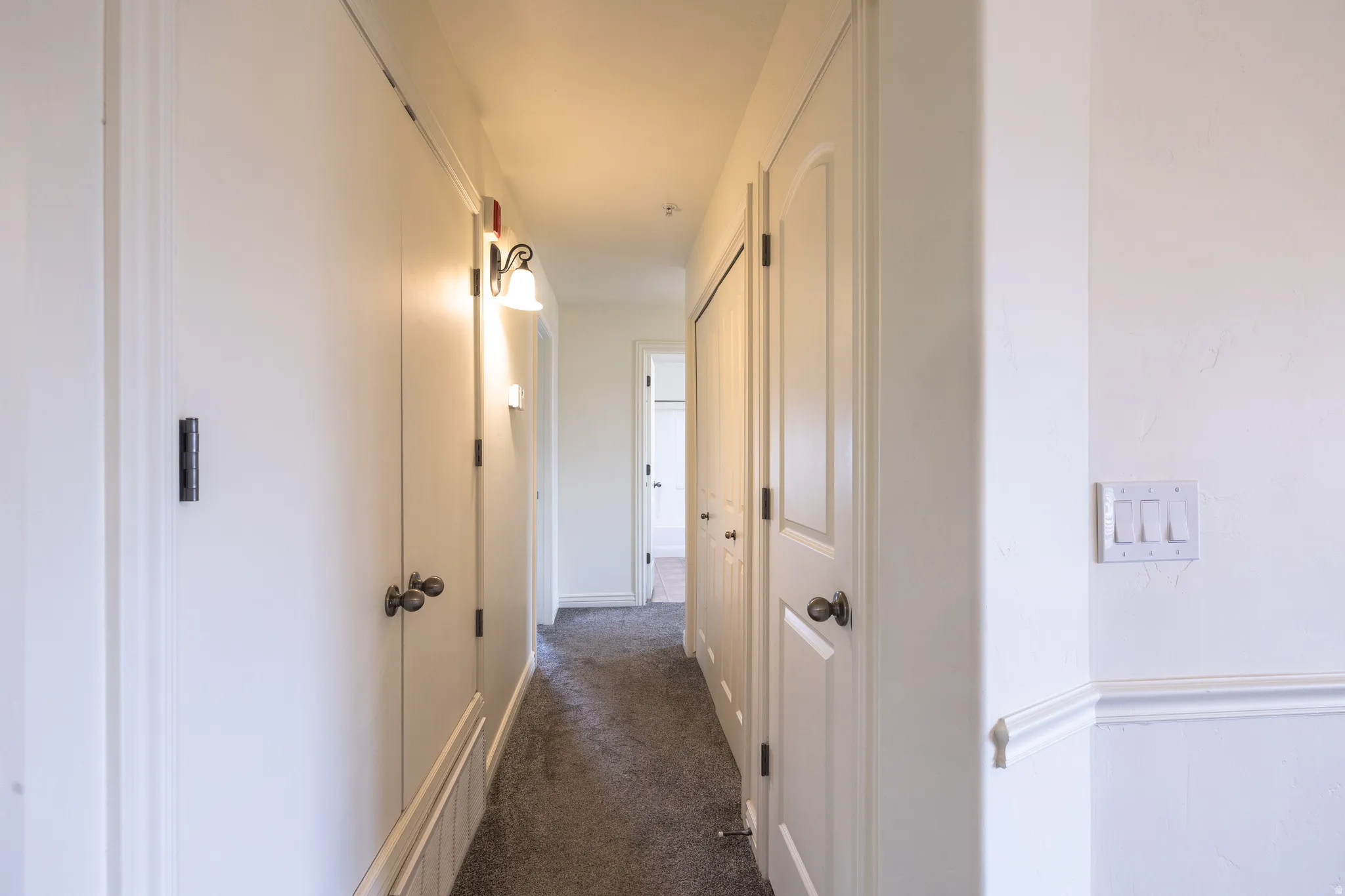 Hallway with light-colored walls, carpeted flooring, and multiple white paneled doors