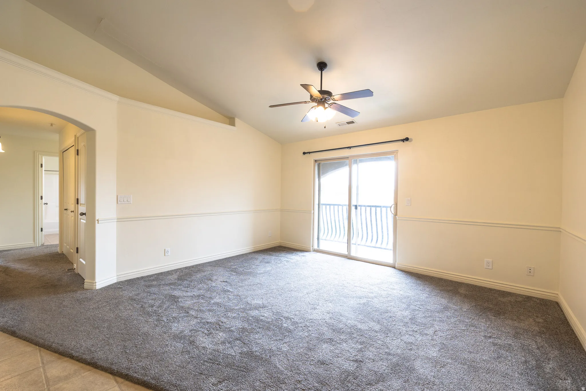 Spacious room featuring vaulted ceilings, a ceiling fan with integrated lighting, and neutral wall tones with decorative wainscoting