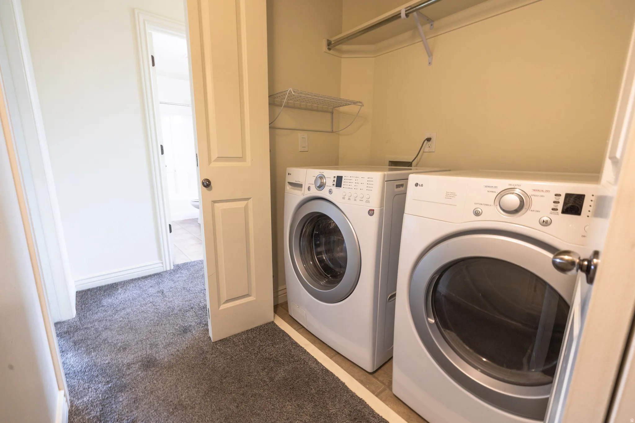 Laundry area featuring tile flooring, neutral wall paint, and a built-in wire shelf with hanging rod