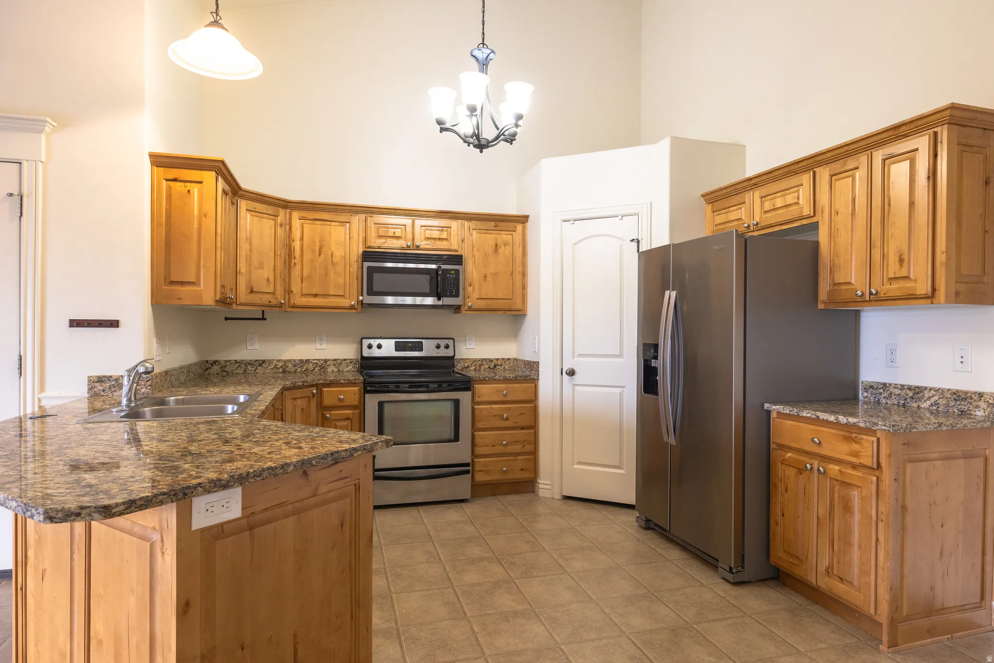 Kitchen featuring wood cabinetry, stainless steel appliances, granite-finish countertops, and tile flooring