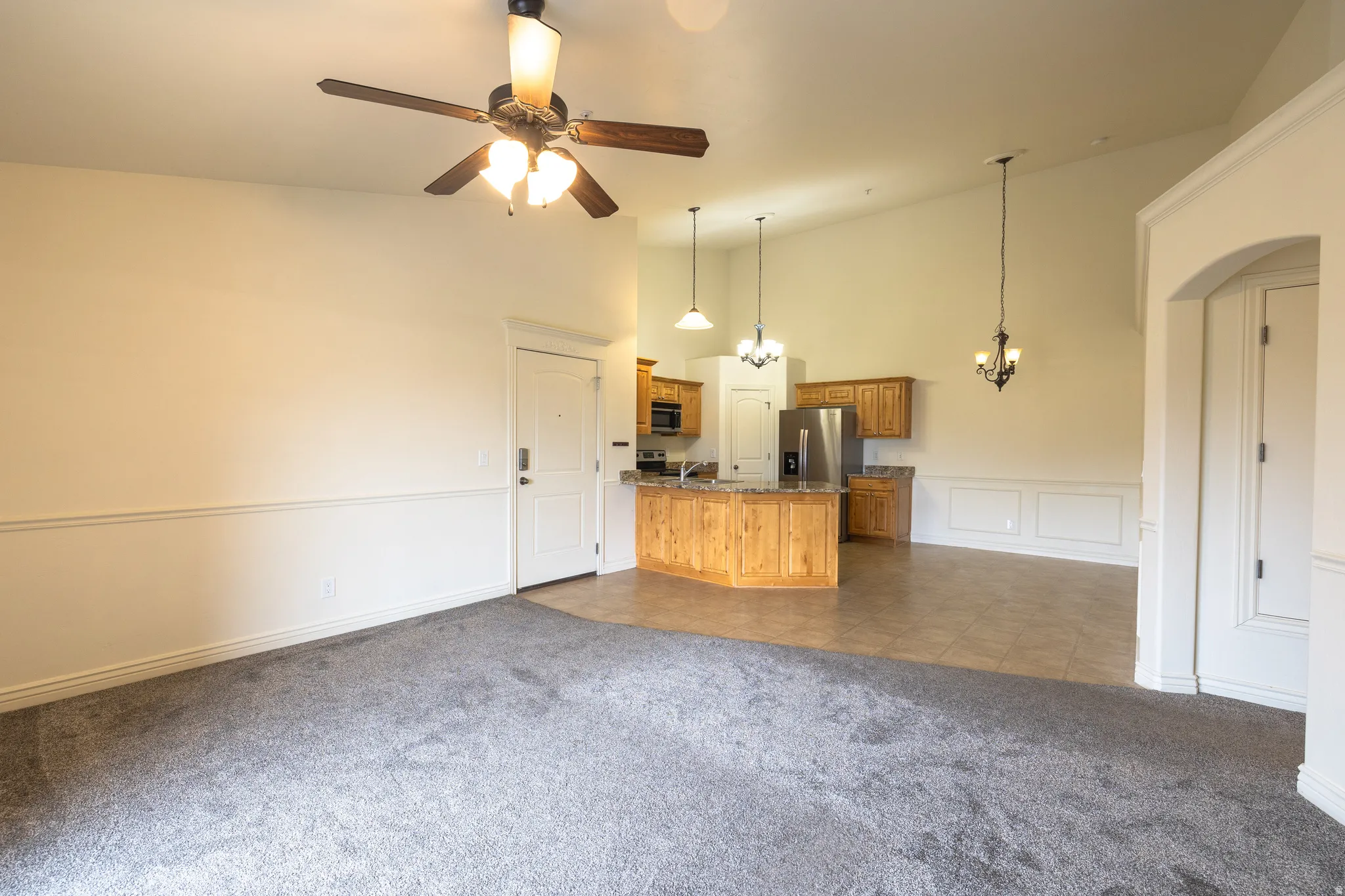 Open-concept living space featuring a carpeted area, a kitchen with wood cabinetry and stainless steel appliances, and tile flooring