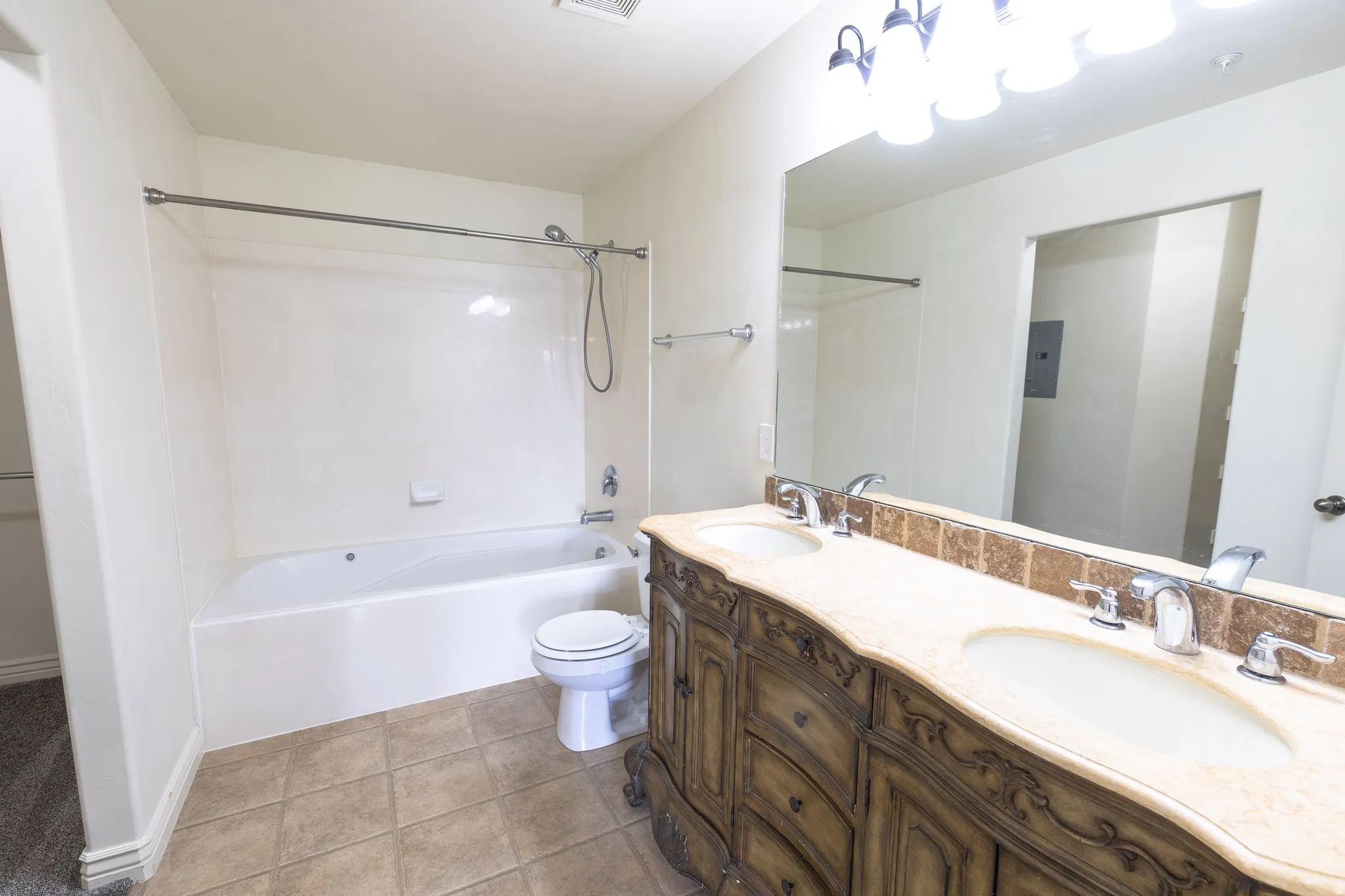 Dual basin vanity with an ornate wood-finish base, light-toned countertop, and square tile backsplash