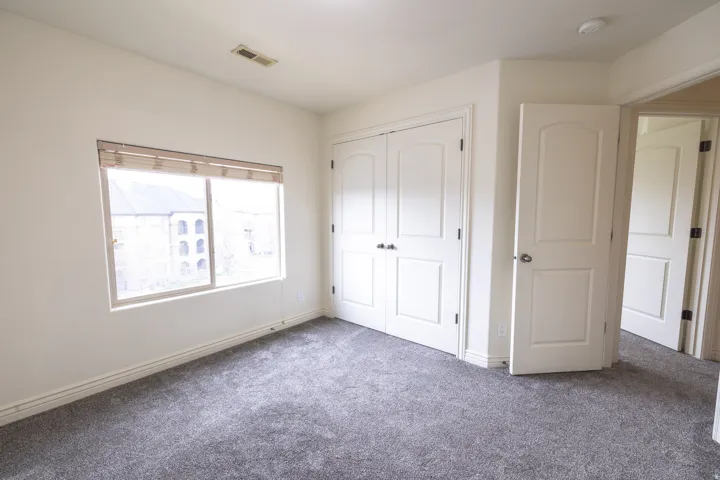 Bright room featuring neutral-toned walls, gray carpeting, a window with horizontal blinds, and a double-door closet with arc-top panels