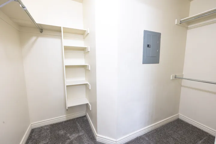 Carpeted walk-in closet featuring built-in shelving, chrome hanging rods, painted baseboards, and a neutral wall finish
