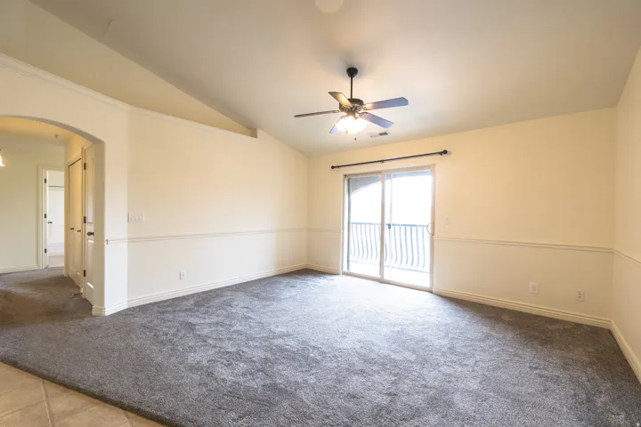 Spacious room featuring vaulted ceilings, a ceiling fan with integrated lighting, and neutral wall tones with decorative wainscoting