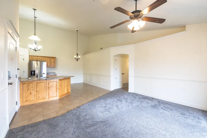 Open concept living area featuring vaulted ceilings, a kitchen island with stone-finish countertops, stainless steel appliances, and a ceiling fan