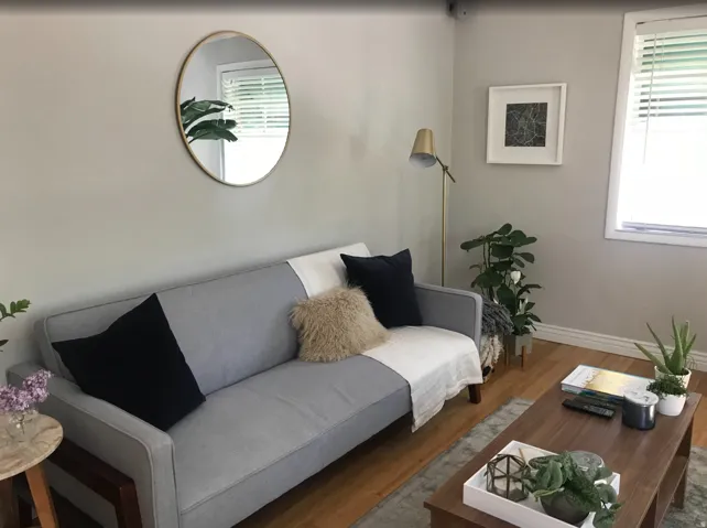 Living area featuring light gray walls, wood-finish flooring, white baseboards, and a window with blinds