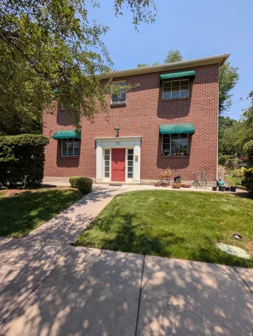 Brick facade residence featuring a red entry door, white door surround, and green window awnings