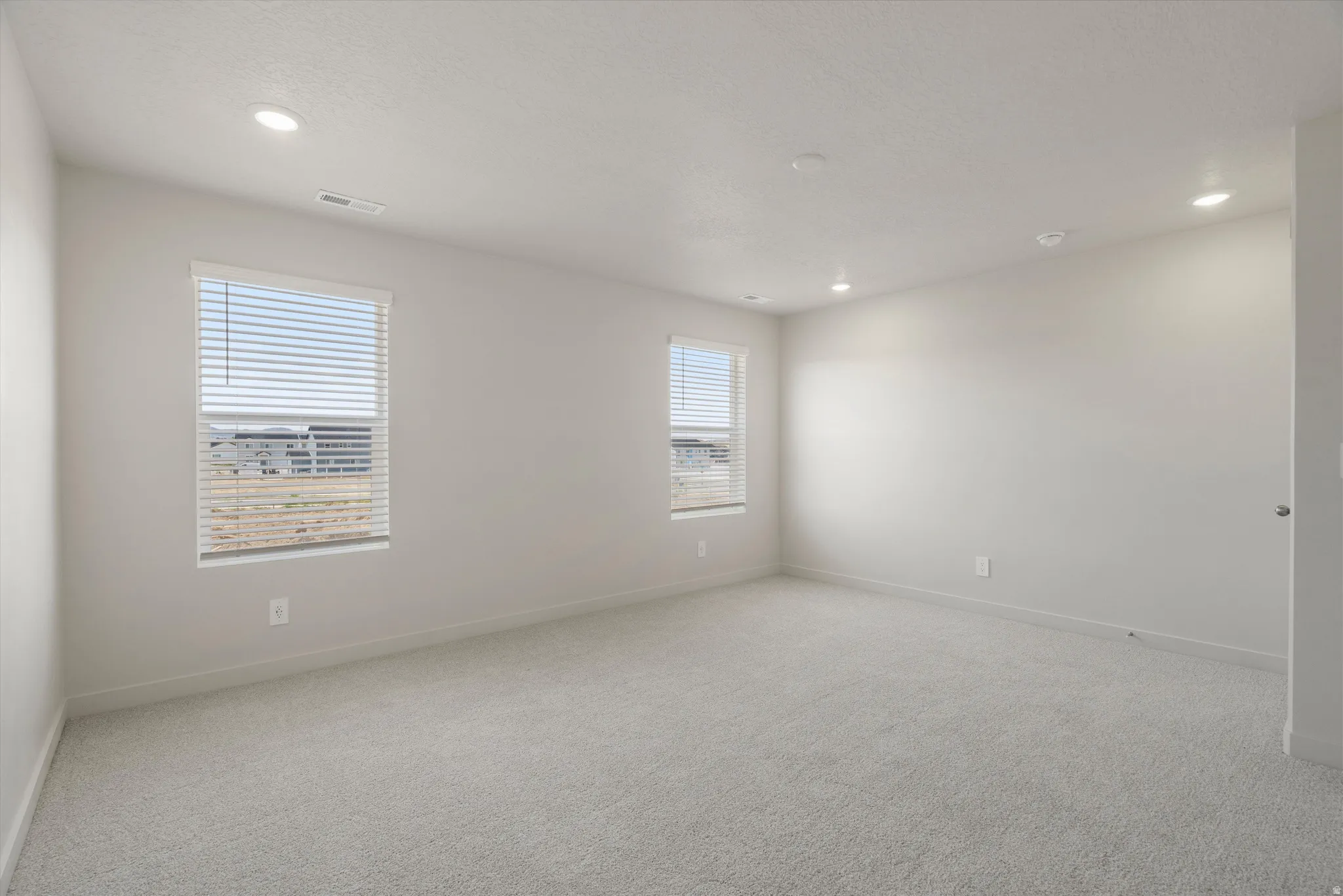 Carpeted room featuring two windows with blinds, recessed lighting, and light-colored walls