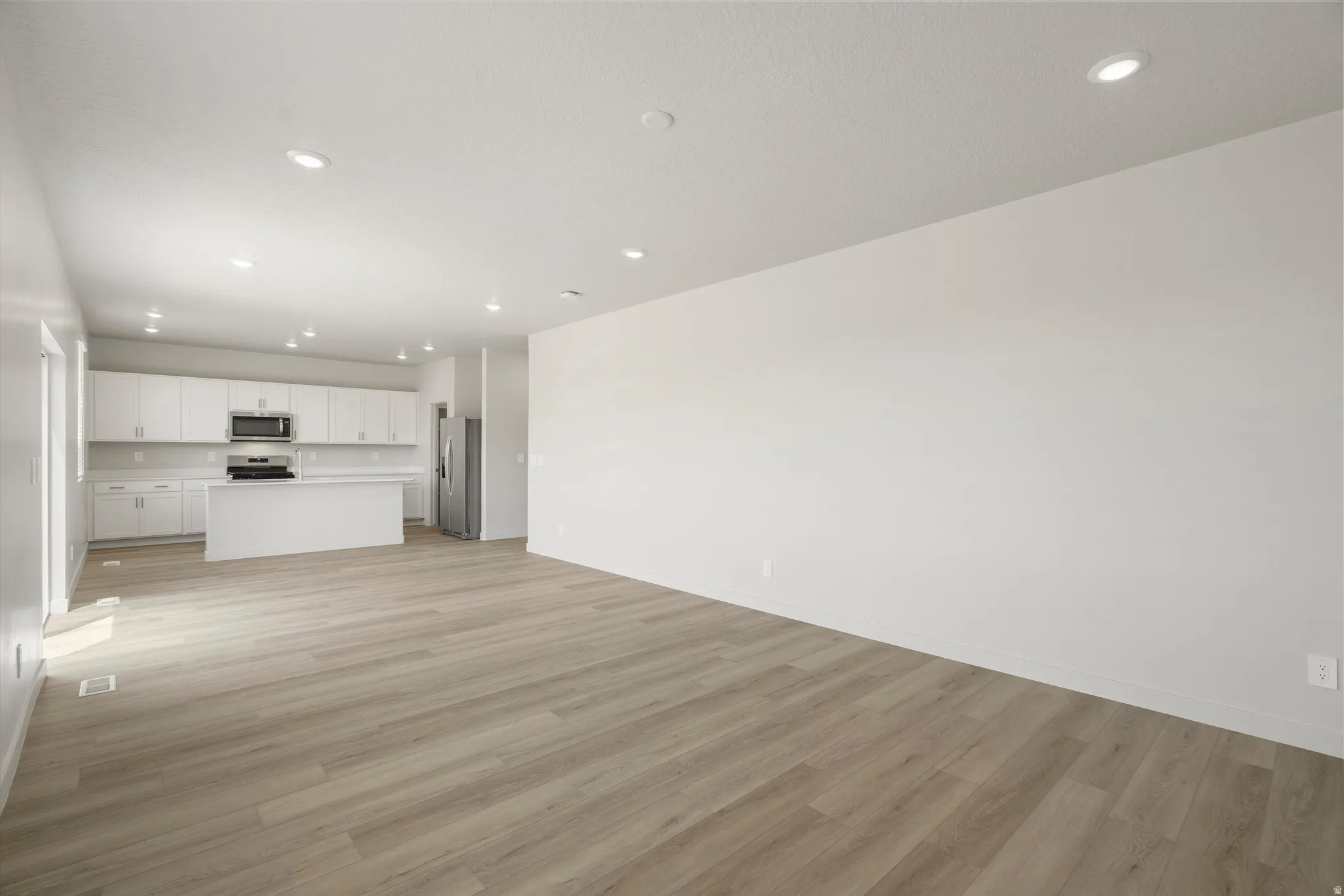 Open-concept living space featuring wood-finish flooring, recessed lighting, and a kitchen with white cabinetry, a central island, and stainless steel appliances