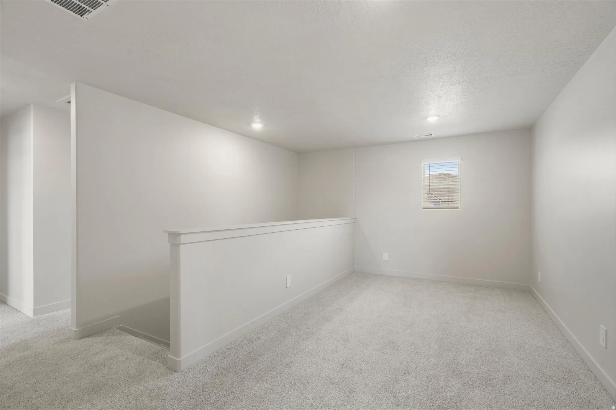 Carpeted room featuring a half-wall partition with white trim, recessed lighting, a single window with blinds, and white painted walls