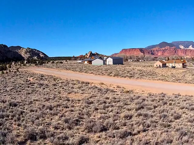Expansive land featuring natural desert vegetation and a dirt road, framed by distant mountains and rock formations