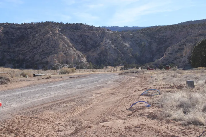 Gravel road entrance amidst a rugged landscape, featuring distant rock formations and a natural terrain backdrop