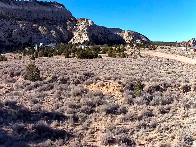 Expansive natural landscape featuring desert vegetation, a gravel road, and distant structures nestled among foothills