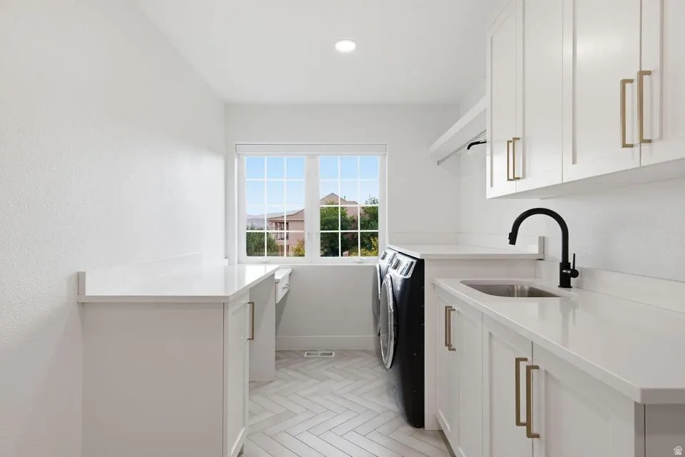 Laundry space featuring white cabinetry, light-toned countertops, a stainless steel undermount sink with a matte black faucet, and herringbone-patterned floor tiles