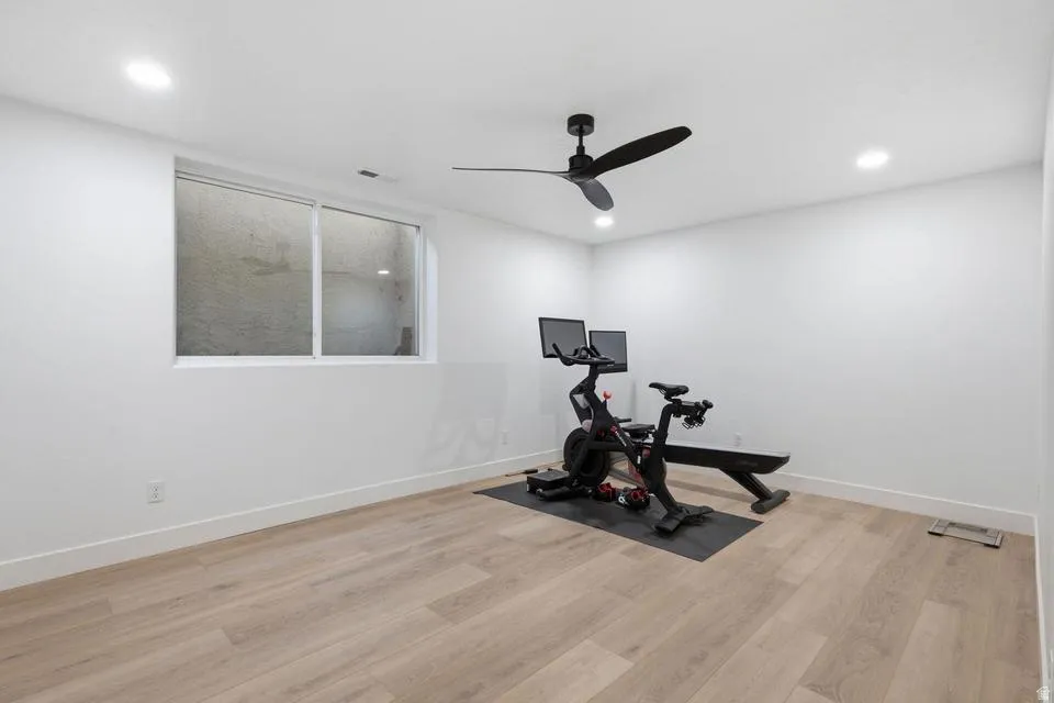 Spacious room featuring light wood-finish flooring, recessed lighting, a ceiling fan with black blades, and a white-framed window