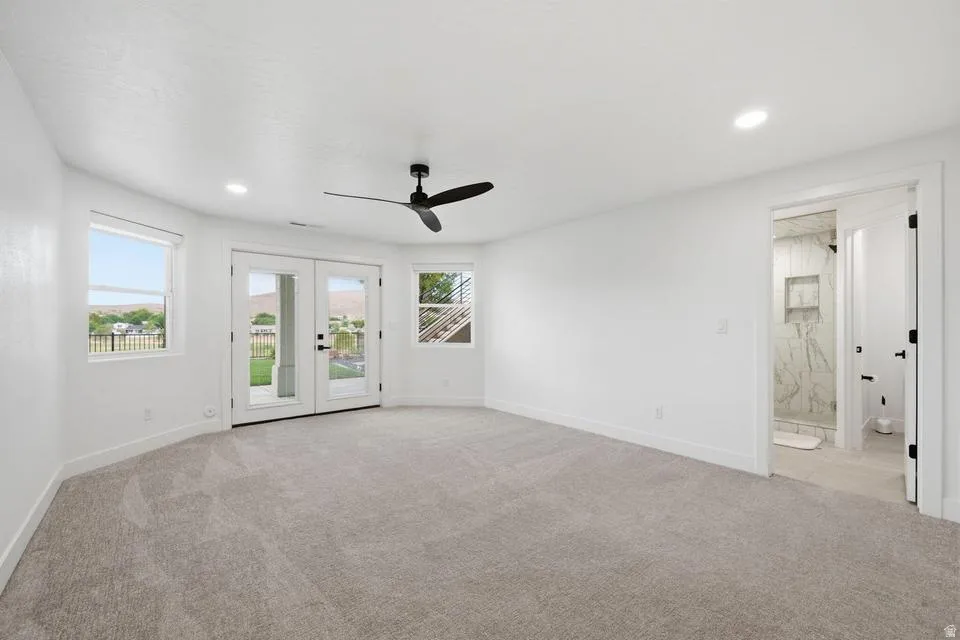 Spacious room featuring light gray carpeting, crisp white walls, recessed lighting, and a modern black ceiling fan