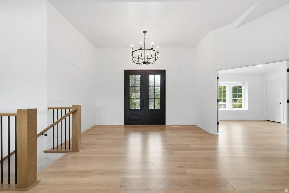 Vaulted entry featuring wood-finish flooring, a contemporary chandelier, and a dark double entry door with frosted glass panels