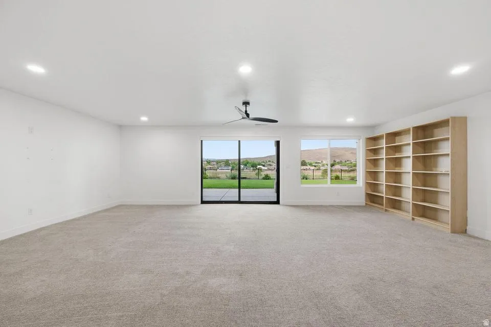 Spacious room featuring light-toned carpeting, white walls, recessed lighting, and a ceiling fan