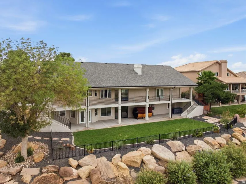 Expansive rear facade featuring a two-story covered patio with a black railing system, a lush green lawn, and a decorative rock-lined perimeter