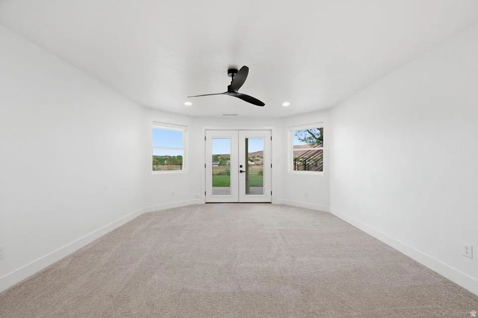 Room featuring light-colored carpet flooring, white walls, and a black ceiling fan with integrated lighting