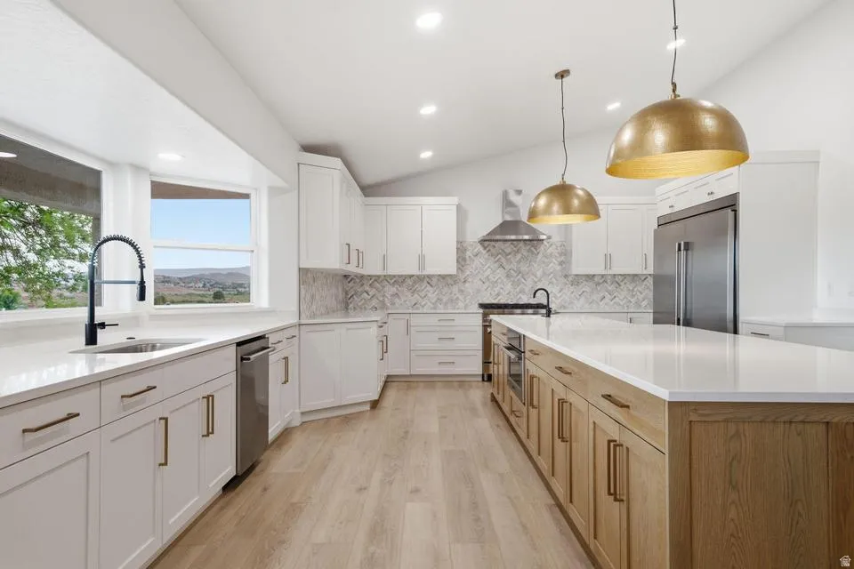 Modern kitchen featuring an expansive island with a light wood-finish base, white countertops, stainless steel appliances, and white shaker-style cabinetry with gold-toned hardware