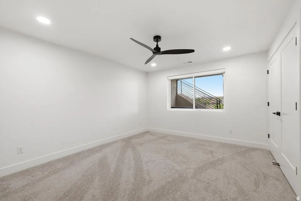 Bright room featuring neutral carpeting, recessed ceiling lighting, a modern black ceiling fan, white baseboards, and a window with a partial exterior railing