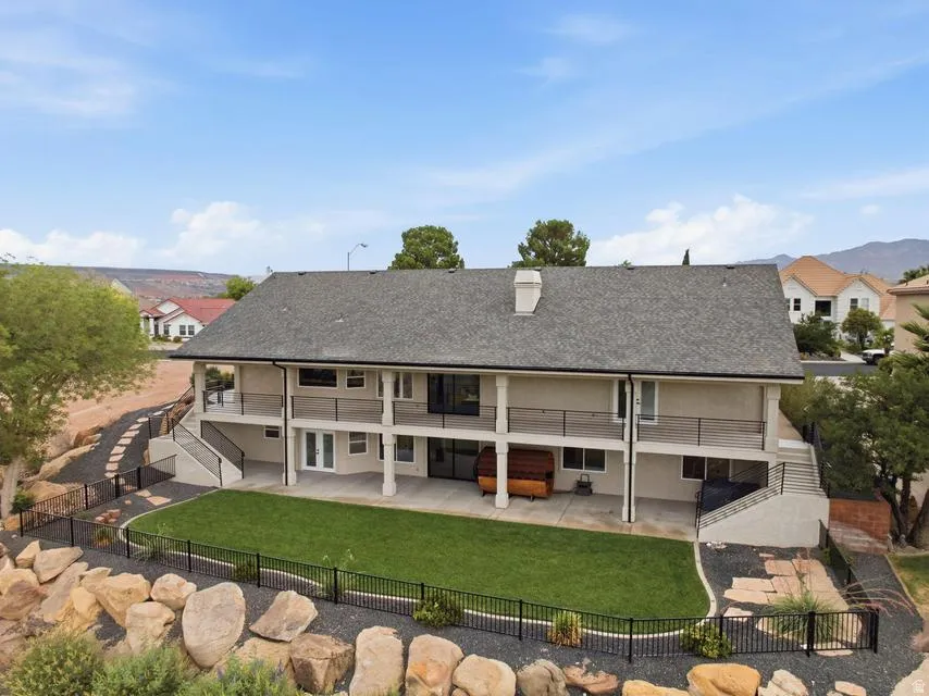 Multi-level rear exterior featuring a ground-level patio, upper-level balcony, and a fenced lawn area