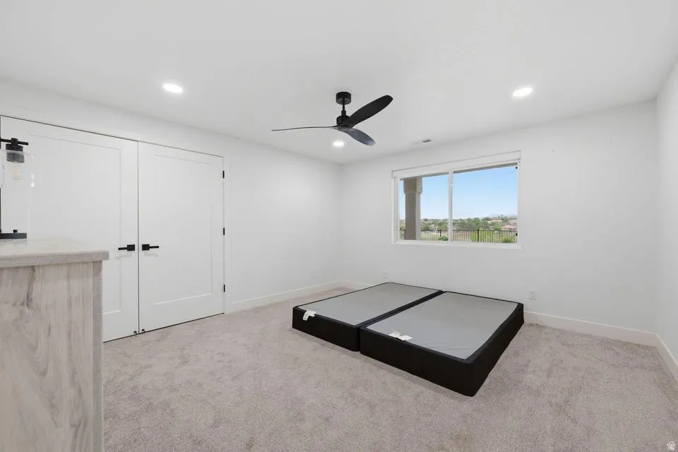 Carpeted room with white walls, a multi-pane window, and a black ceiling fan