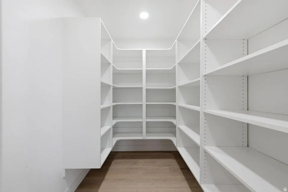 Walk-in pantry featuring extensive white built-in shelving, wood-finish flooring, and recessed ceiling lighting