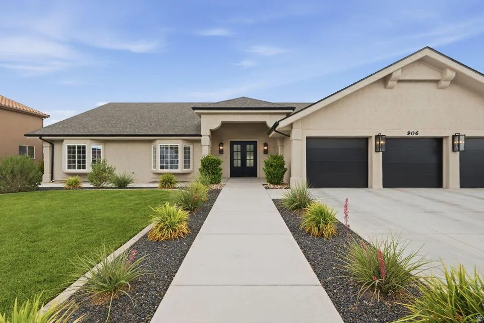 Contemporary stucco exterior featuring a two-car garage with black doors, a covered entry with dual dark-framed glass doors, and multiple bay windows