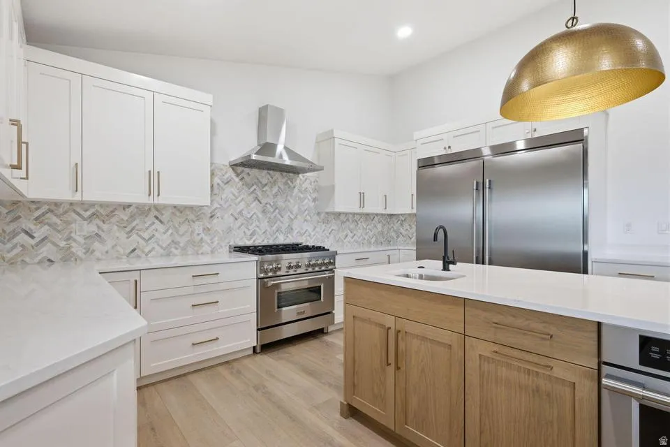 Modern kitchen featuring white shaker cabinetry, stainless steel appliances, a herringbone tile backsplash, an oversized island with a built-in sink, and wood-finish flooring