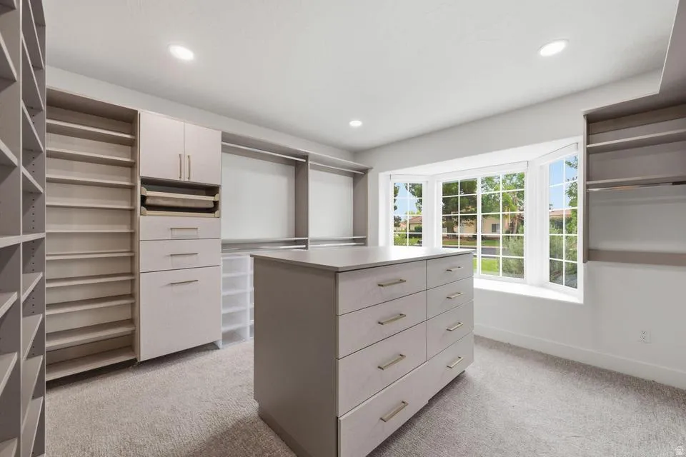 Spacious custom closet featuring extensive built-in shelving, an integrated storage island with drawers, hanging rods, recessed lighting, and a multi-paned bay window