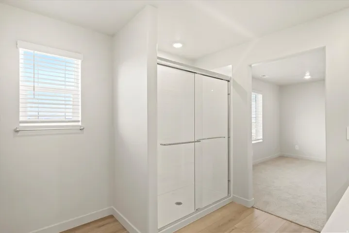 Enclosed shower with sliding glass doors, recessed lighting, and a neutral white finish