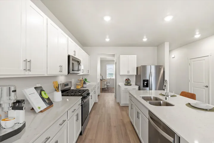 Bright kitchen featuring white shaker cabinetry, stainless steel appliances, light-toned countertops, a center island with double sink, and wood-finish flooring