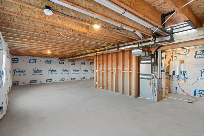 Unfinished basement featuring exposed wood joists, concrete flooring, and a framed utility area with visible ductwork and a tankless water heater